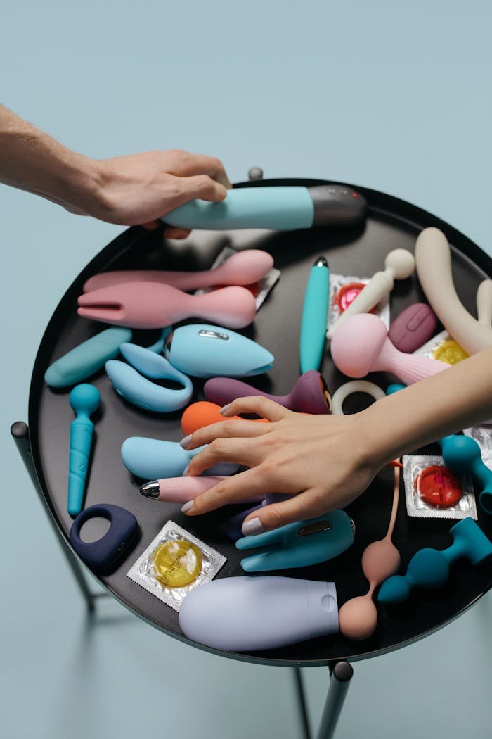 Hands reaching for diverse sex toys on a modern black table.